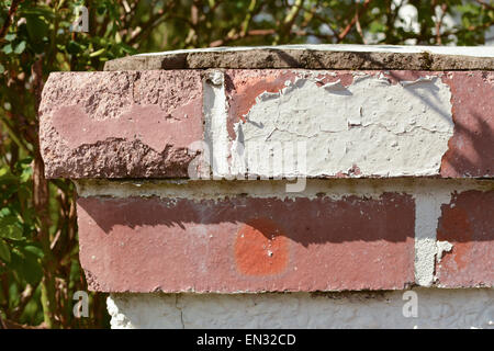 paint peeling off due to weathering - red brick garden wall gatepost cap requiring maintenance and repainting Stock Photo