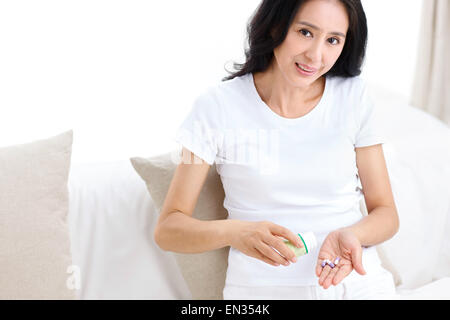 The middle-aged woman holding a capsule leaned on the bed Stock Photo