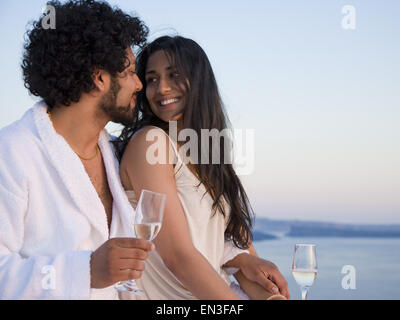 Couple sitting outdoors with champagne flutes and scenic background smiling and snuggling Stock Photo