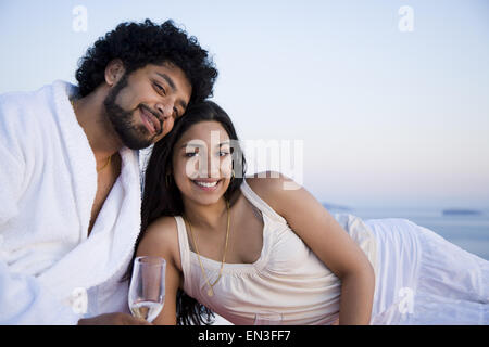 Couple sitting outdoors with champagne flutes and scenic background smiling and snuggling Stock Photo