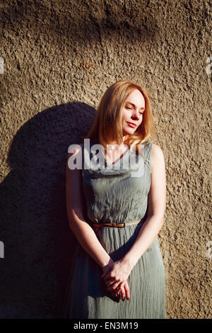 Fashion portrait of young attractive woman near grey wall. Blonde hair, sunset. Timeless style. Stock Photo