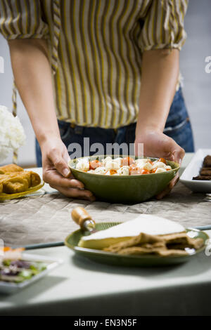 Woman holding tray of sushi with other foods and flower arrangement Stock Photo