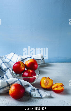 Five ripe nectarines on blue background with checked kitchen towel. Vertical composition. Selective focus. Stock Photo
