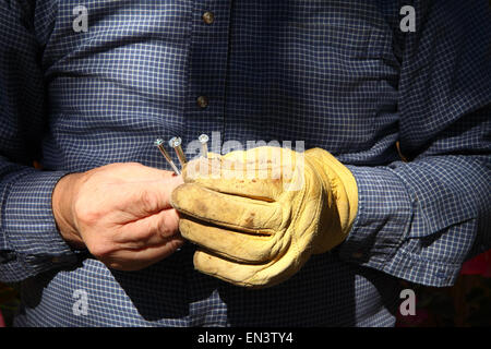 A man working outdoors holds three screws in his hands. Stock Photo