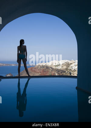 Woman in swimsuit standing at edge of infinity pool rear view Stock Photo