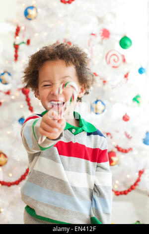 Happy young boy with candy stick posing in front of Christmas tree Stock Photo