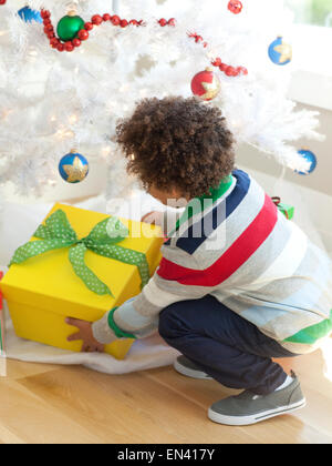 Young boy picking up Christmas present from under Christmas tree Stock Photo