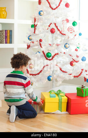 Young boy sitting under Christmas tree, picking up Christmas presents Stock Photo