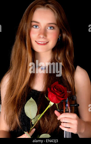 A pretty woman standing isolated for black background holding her violin and a red rose. Stock Photo