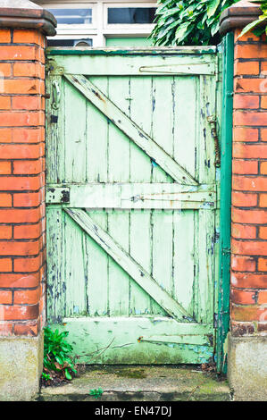 A weathered wooden garden gate in a red brick wall in the UK Stock Photo