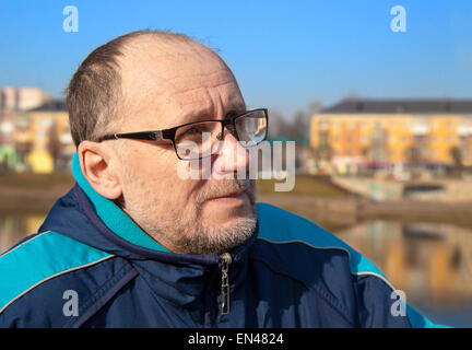 portrait of elderly man wearing glasses and a blue jacket in a city park Stock Photo