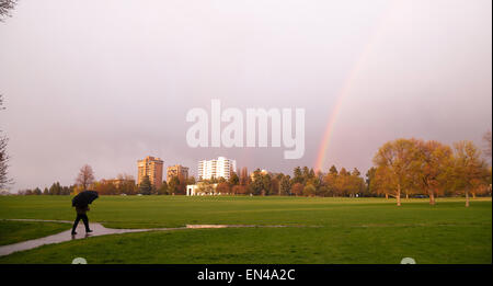 The sun peaks through for a moment lighting the way and producing a rainbow near a person walking with umbrella Stock Photo