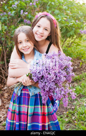 Two girls hug holding bouquet of Lilac flowers Stock Photo