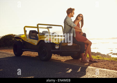 Loving young couple sitting on the hood of their car while out on a roadtrip. Caucasian young couple relaxing together on their Stock Photo