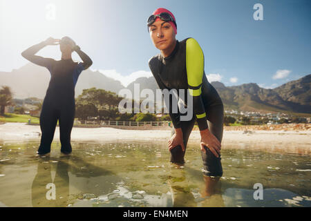 Confident young woman in wet suit standing in water looking at camera. Young triathletes preparing for competition. Triathlon tr Stock Photo