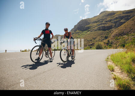 Two young athletes taking a break from cycling on country road. Cyclist training for triathlon competition on open road with bic Stock Photo