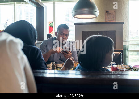 A man uses his smartphone while having lunch with his family in Kuala Lumpur, Malaysia. Stock Photo