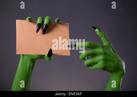 Green monster hands with black long nails pointing on blank piece of cardboard, Halloween theme Stock Photo