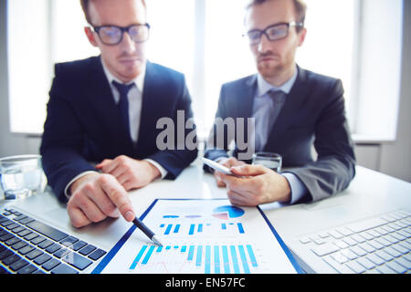 Confident businessman analyzing chart and explaining it to co-worker Stock Photo