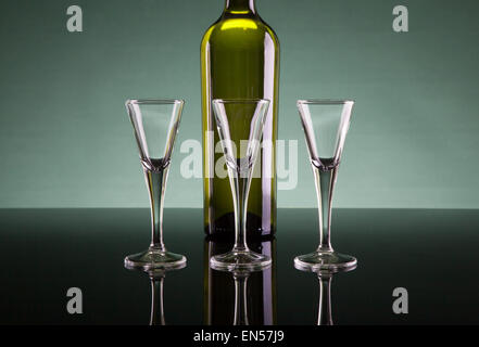 Shot glasses and a bottle on a black polished surface with a greenish background