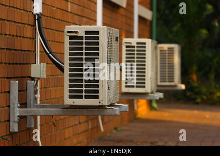 Three external air-conditioner units mounted outside on a wall, focus on the first unit. Stock Photo