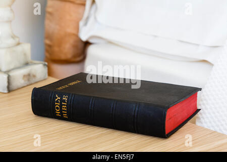 English Holy Bible book on a bedside table beside a bed in a bedroom. England, UK, Britain, Europe Stock Photo