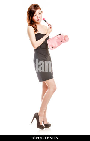 Chinese woman in black dress putting on makeup, holding pink make-up bag Stock Photo