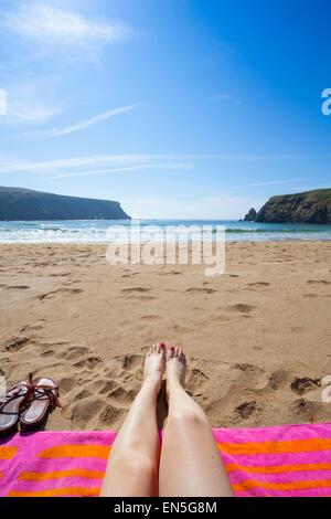 Legs on a colourful beach towel on a sandy beach with view of the sea Stock Photo