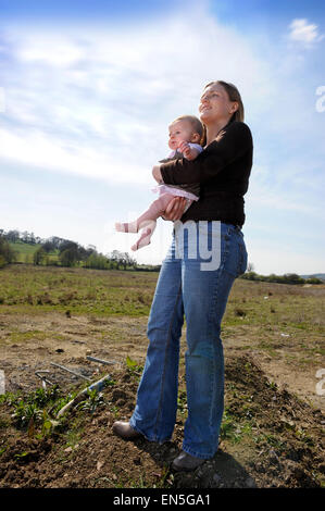 Young mother and baby on a brownfield site with adjoining Newbuild housing earmarked for development UK Stock Photo