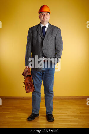 Male engineer, inspect the room and he holds old leather briefcase, parquet floor and yellow wall Stock Photo