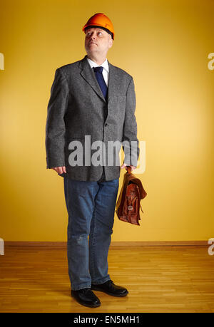 Male engineer, inspect the room and he holds old leather briefcase, parquet floor and yellow wall Stock Photo