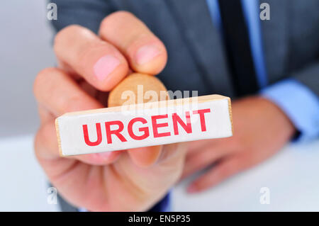 a young caucasian man at his office desk with a rubber stamp with the word urgent Stock Photo