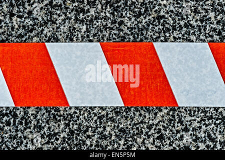 Closeup view of the do not cross warning tape of red and white color fixed to the block of gray and black granite stone. Stock Photo