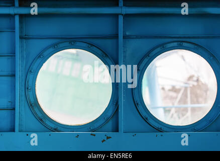 Two metal portholes with bolts on painted blue metal background. Inside view of the old aircraft. Stock Photo
