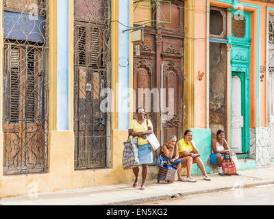 Four Cuban ladies, three of whom are sitting, in front of old historic facades of buildings with intricate wood carvings on the Stock Photo