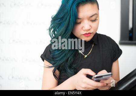 Asian woman with blue hair texting on smartphone