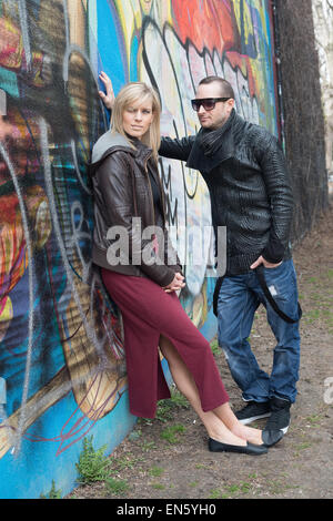Young couple leaning against wall with graffiti looking unhappy Stock Photo