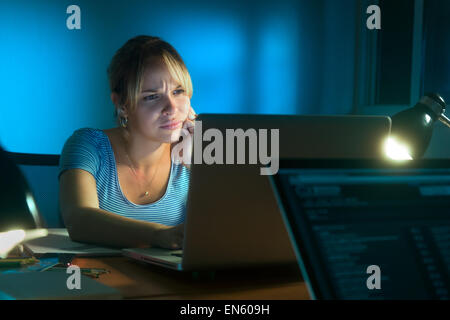 Beautiful woman working late at night, looking at laptop monitor with hand on chin, having problems to understand what she sees. Stock Photo