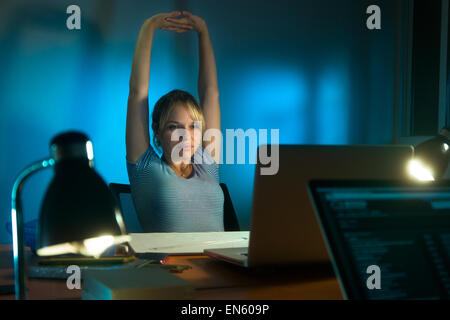 Beautiful woman working as interior designer, staying late at night in office with drawings and laptop computer to complete a pr Stock Photo