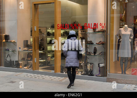 The girl in a gray jacket and a cap stands near shop and looks at goods. Stock Photo