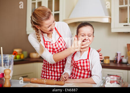 Laughing girl and her mother in aprons having fun in the kitchen Stock Photo