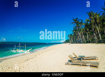 lounge chairs and traditional boat on tropical puka beach in boracay philippines Stock Photo