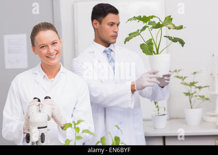 Scientist smiling at camera while colleague looking at plant Stock Photo