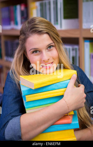 Pretty student in library with pile of books Stock Photo - Alamy
