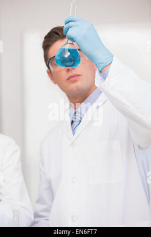 Scientist looking at beaker with blue fluid Stock Photo