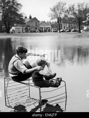 Two boys sitting on an old fire guard on the edge of a lake. 1st July 1955 Stock Photo