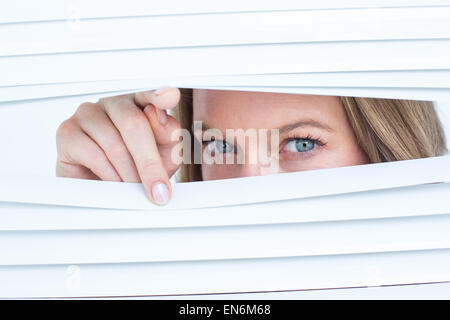 Woman peering through roller blind Stock Photo