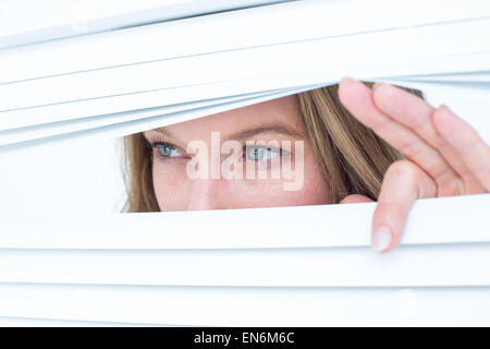 Woman peering through roller blind Stock Photo