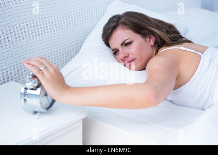 Pretty woman extending hand to alarm clock in bed Stock Photo