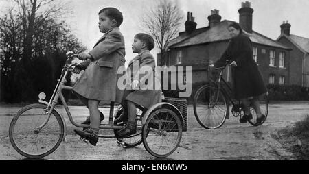 When Mrs. Nora Moore of Wokingham Road, Bracknell, Berkshire, goes off for her Christmas shopping on her cycle she has two able assistants and carriers in her two children David, aged 4 yrs, and Alan aged 3 yrs, who act as transport by means of a large ba Stock Photo